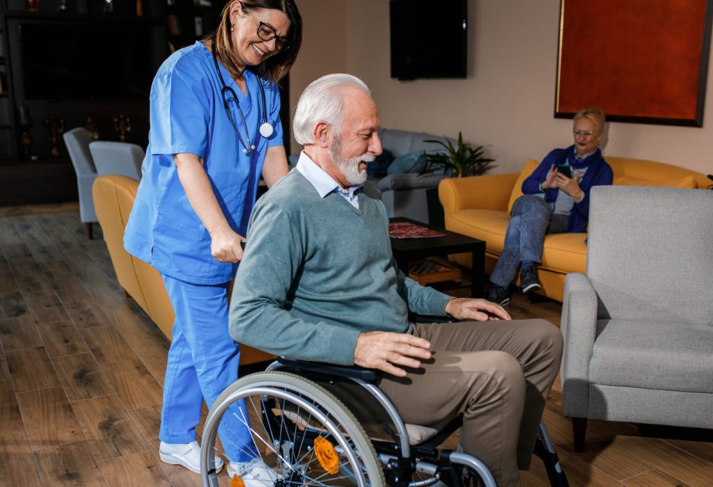 Female nurse assisting senior man in a wheelchair at nursing home.
