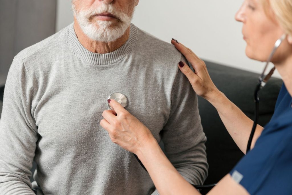 Clinician listening to chest home visit Clinician listening to an older adult’s chest with a stethoscope during a home visit